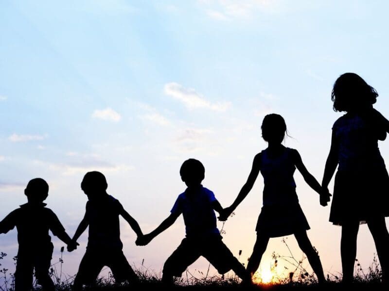 Children in silhoutte holding hands across a field.