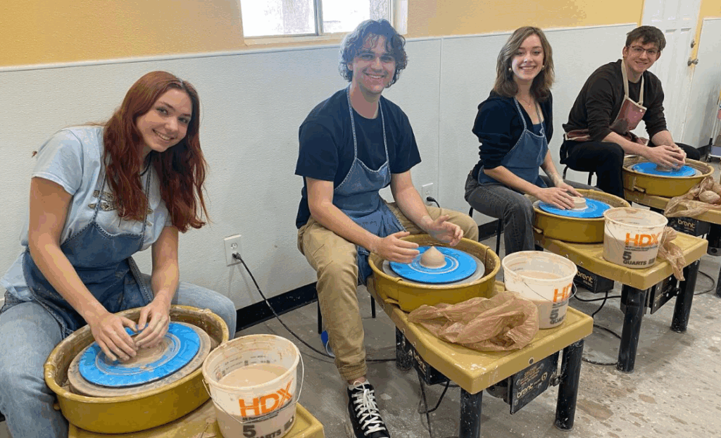Group of potters sitting behind pottery wheels at Sunshine Sunflower Studios.