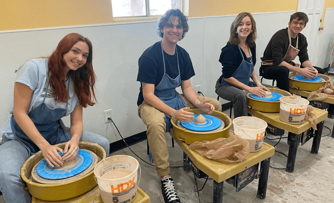 Group of potters sitting behind pottery wheels at Sunshine Sunflower Studios.